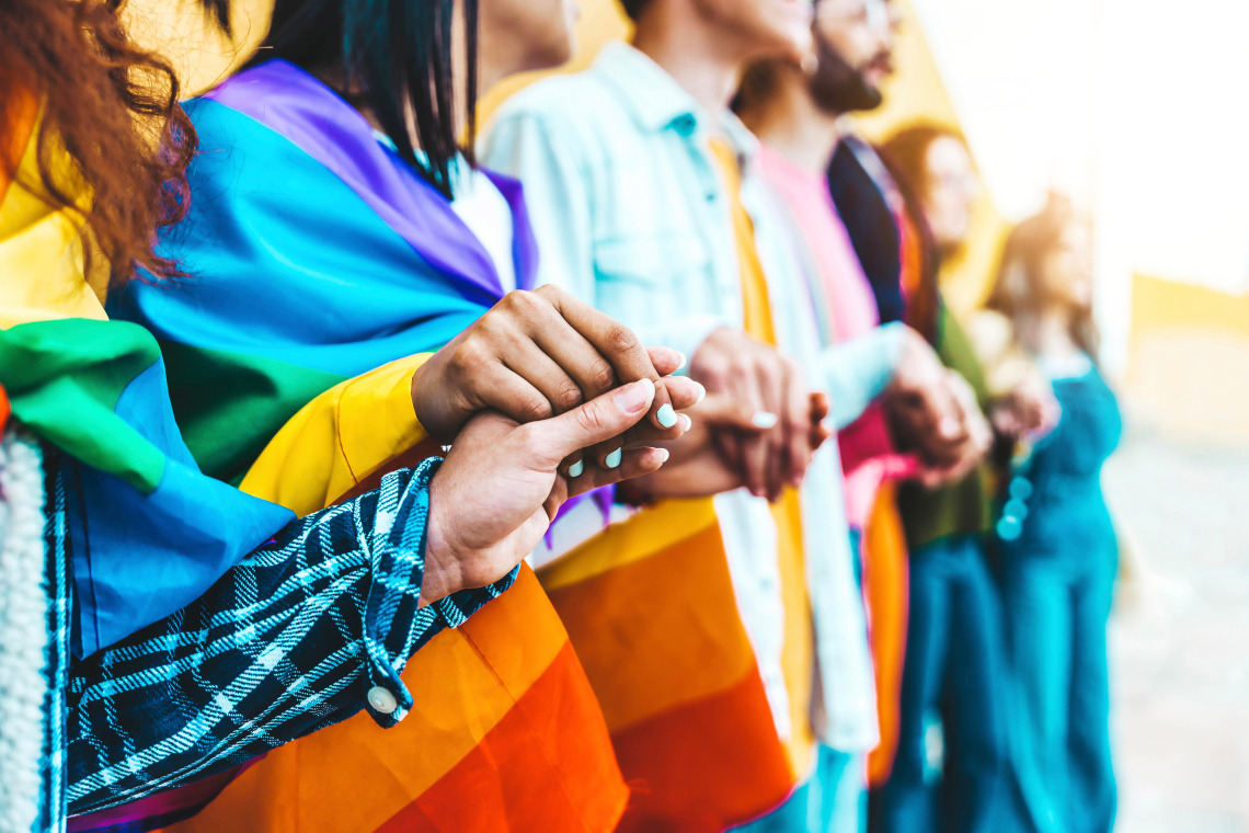 Picture of people holding hands wearing a rainbow flag